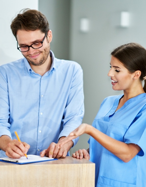 Dental team member showing a patient where to sign on clipboard