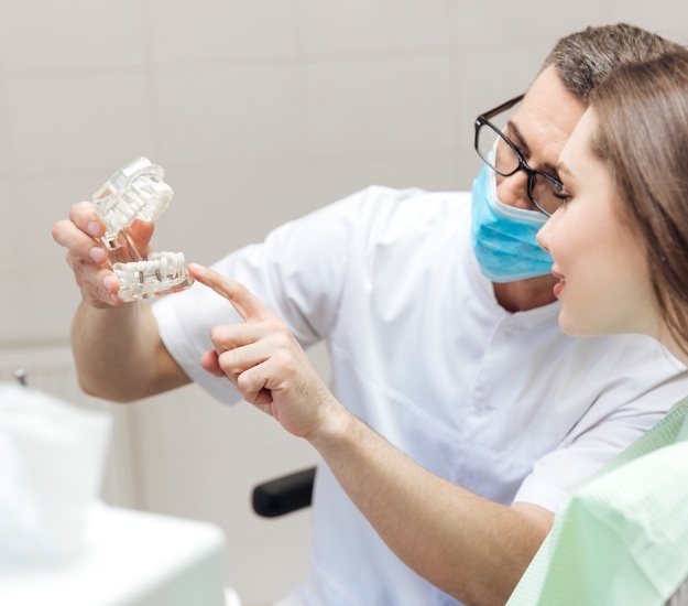 Dentist showing a model of a mouth with a dental implant to a patient