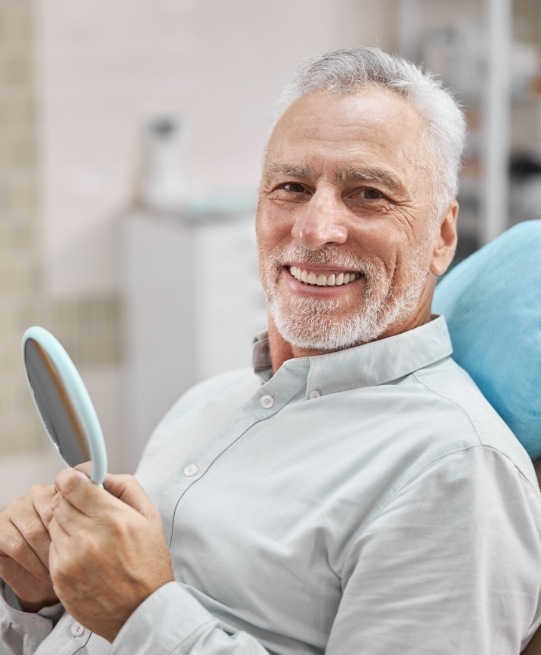 Smiling senior man holding mirror while visiting Arlington Heights dentist