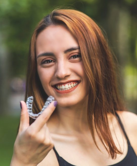 Smiling woman holding an Invisalign clear aligner in Arlington Heights