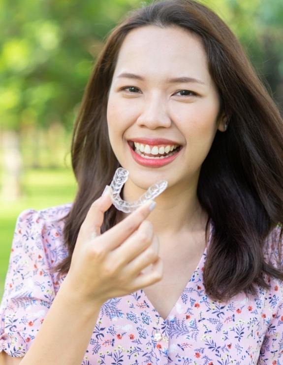 Smiling woman holding Invisalign tray outdoors