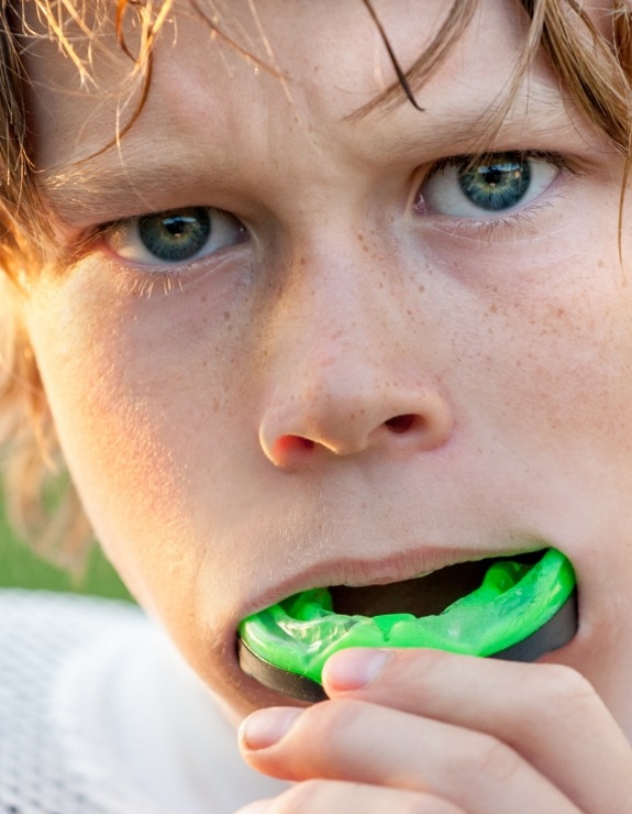 Young boy placing green athletic mouthguard into his mouth