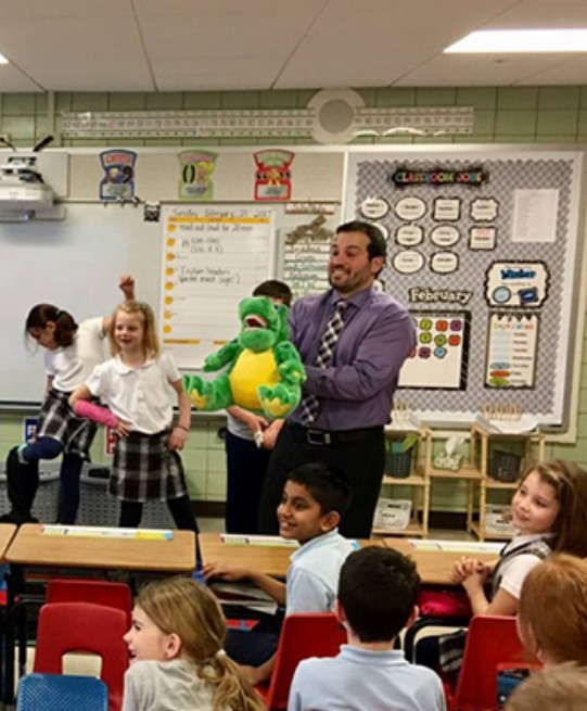 Arlington Heights dentist holding dinosaur plush while giving presentation to classroom