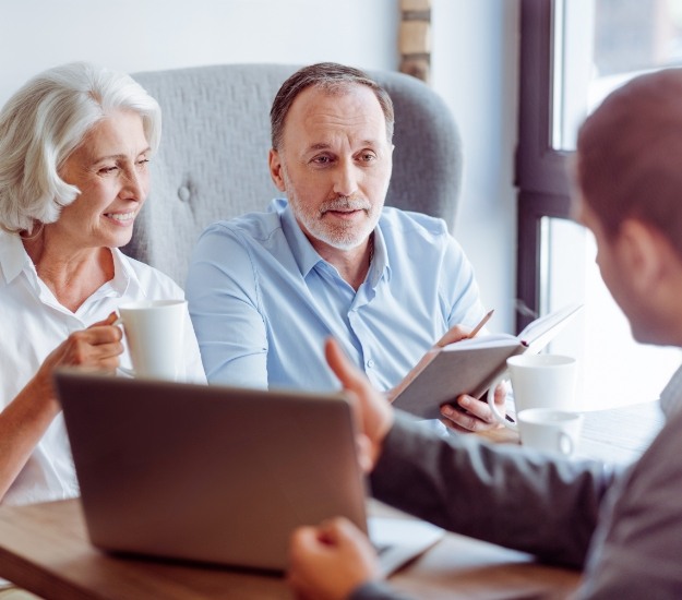 Senior couple talking to man across desk with laptop