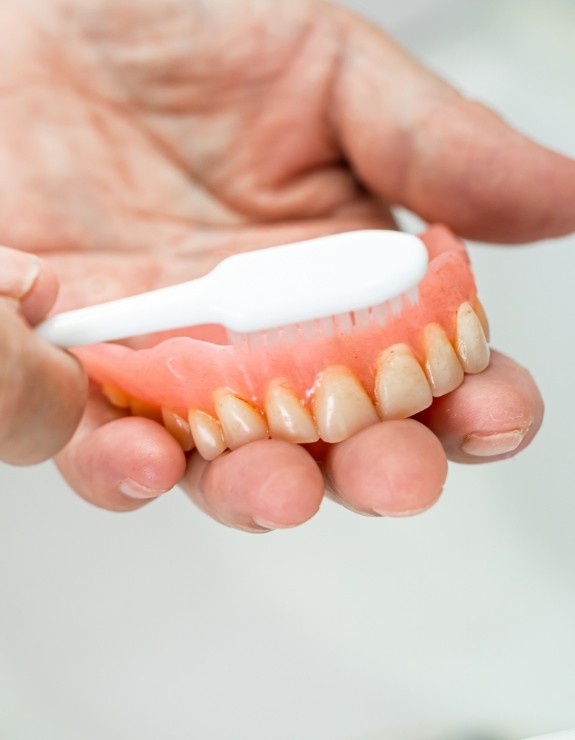 Person cleaning their denture with a toothbrush