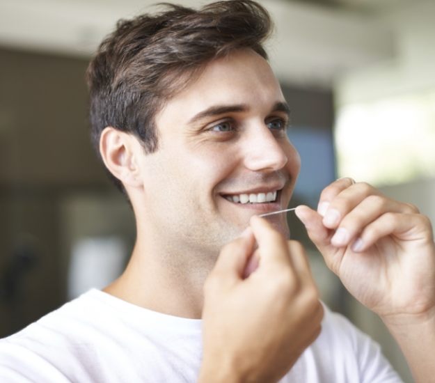 Smiling man flossing his teeth