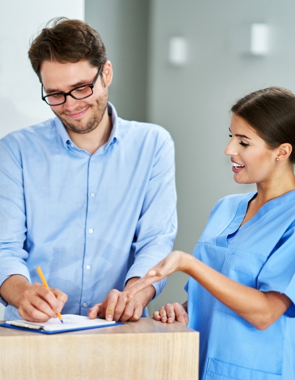 Dental team member showing patient where to sign on clipboard