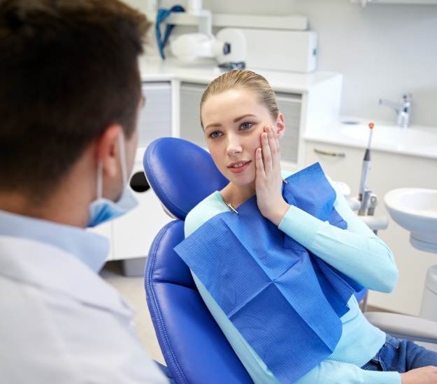 Young woman holding cheek in pain while talking to dentist