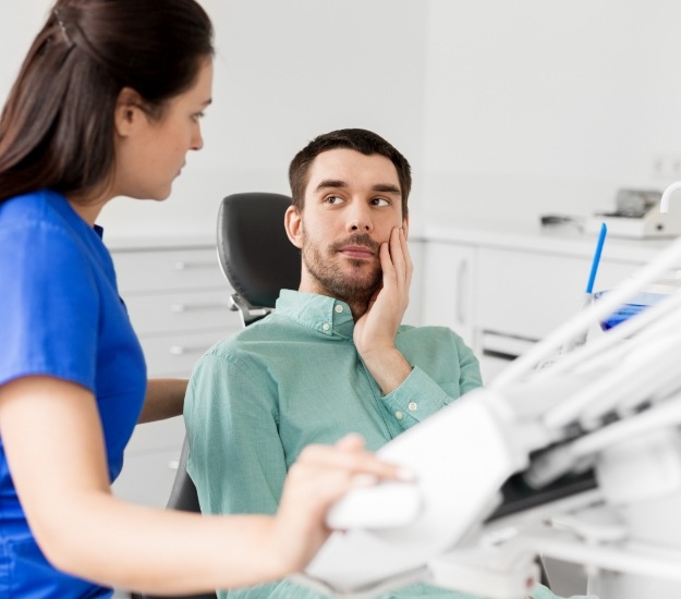 Worried man in dental chair holding his cheek