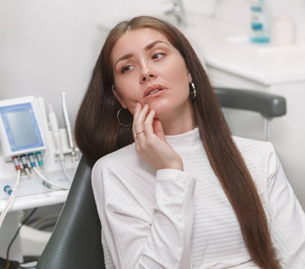 Woman in white sweater holding her cheek in pain