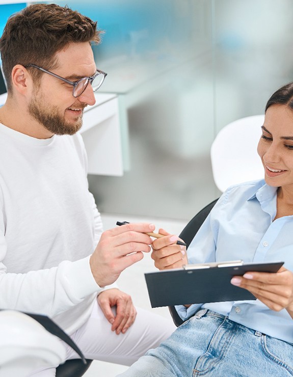 Man giving woman in dental chair insurance forms on clipboard