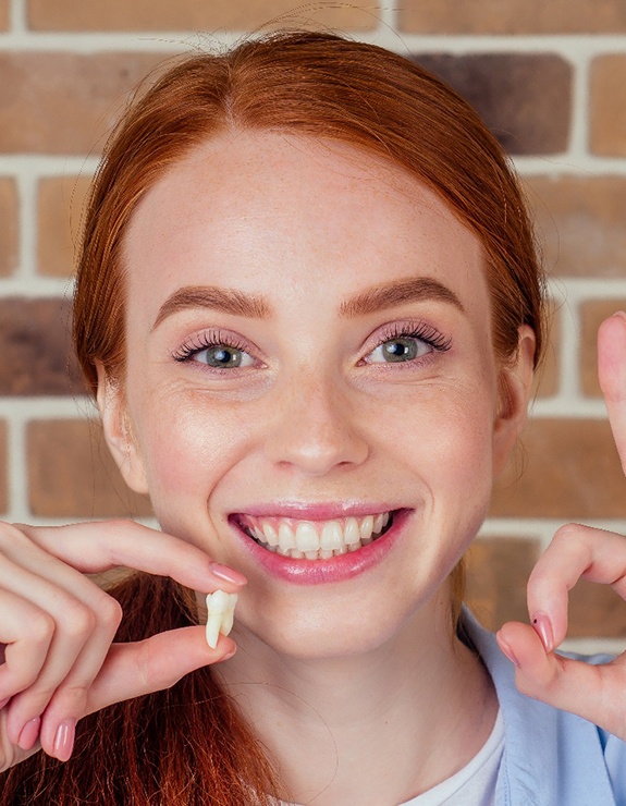 Woman holding extracted tooth with one hand and making ‘ok’ sign with the other