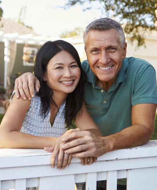 Man and woman smiling in their front yard after replacing missing teeth in Arlington Heights