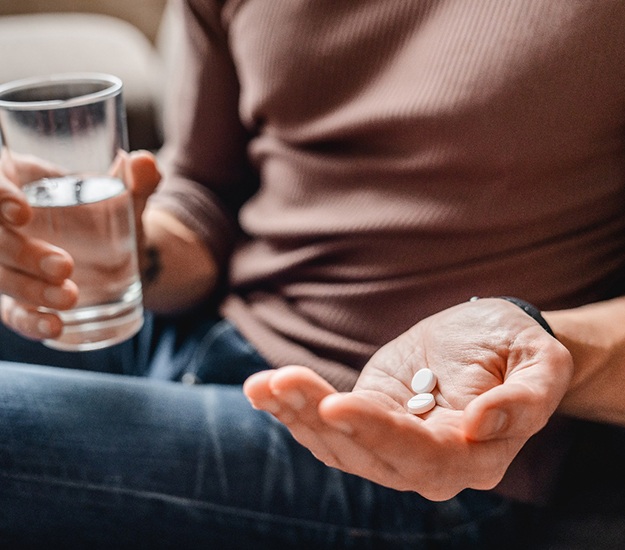 Hand holding glass of water and the other holding two pills