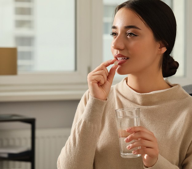 Woman in beige sweater taking pill with glass of water
