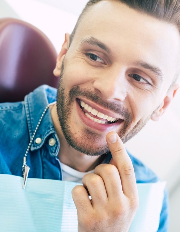 Man in dental chair pointing to his smile