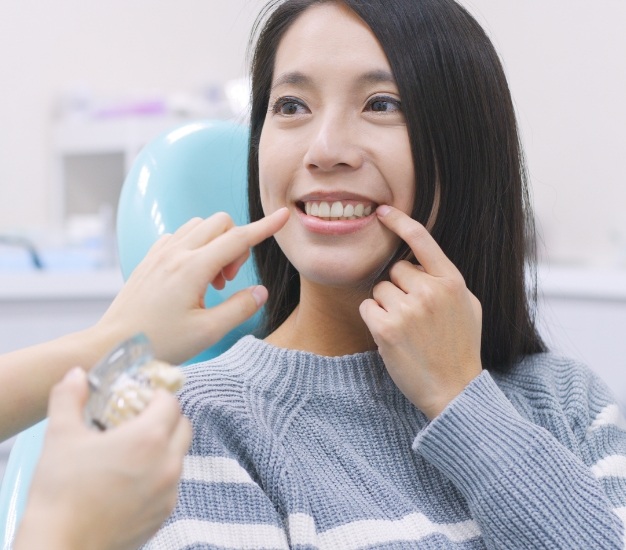 Woman in dental chair pointing to her smile