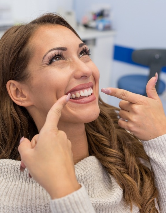 Woman in dental chair pointing to her smile