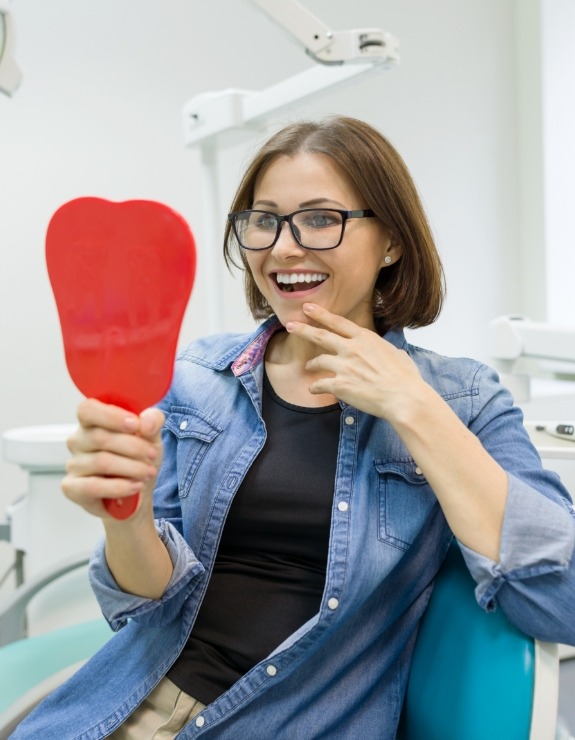 Dental patient in denim jacket admiring her smile in mirror