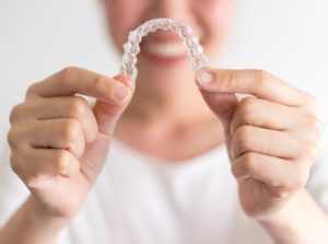 Smiling woman holds out set of Invisalign in Arlington Heights