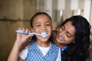 a child brushing her teeth with her mother