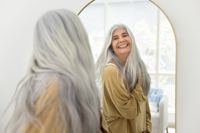 Older patient smiling in mirror after cosmetic dentistry