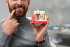 man holding a model of a dental implant and pointing to his own smile